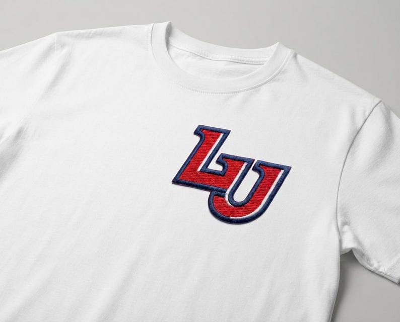 May include: A white short-sleeved t-shirt featuring an embroidered patch on the left chest. The patch displays the letters LU in a bold, stylized font, rendered in red with a thick navy blue outline and a white inner border detail.