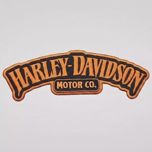 May include: An embroidered patch featuring the Harley-Davidson Motor Co. logo in orange and black. The text Harley-Davidson is arched across the top, with Motor Co. centered below in a rectangular section, all outlined in orange thread.