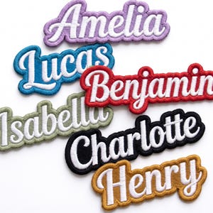 May include: A collection of six embroidered name patches featuring the names Amelia in purple, Lucas in blue, Benjamin in red, Isabella in sage green, Charlotte in black, and Henry in gold. Each patch has white cursive lettering with a matching border.