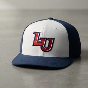 May include: A baseball cap featuring a white front panel and navy blue side and back panels. The front displays an embroidered red and navy blue logo with the letters LU. The cap has a navy blue brim and a button on the top center.