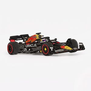May include: A black and dark blue Formula 1 race car model featuring red and yellow Red Bull branding, Oracle text, and Mobil logos. The vehicle has black tires with red rims, a yellow nose cone, and a detailed cockpit with a driver figure inside.