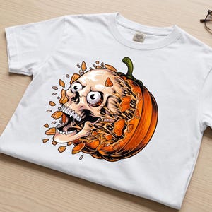 May include: A white short-sleeved t-shirt featuring a graphic print of a human skull bursting out from the centre of a bright orange pumpkin. The skull has wide eyes and an open mouth, surrounded by scattered orange pumpkin shards.