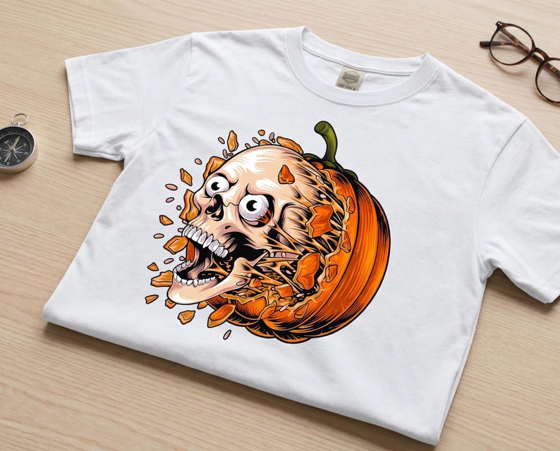 May include: A white short-sleeved t-shirt featuring a graphic print of a human skull bursting out from the centre of a bright orange pumpkin. The skull has wide eyes and an open mouth, surrounded by scattered orange pumpkin shards.