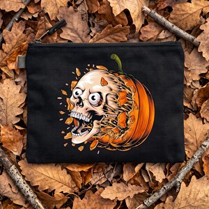 May include: A black zipped pouch featuring a graphic illustration of a human skull emerging from a bright orange pumpkin. The skull has wide eyes and an open mouth, with orange pumpkin fragments appearing to explode outwards from the centre.