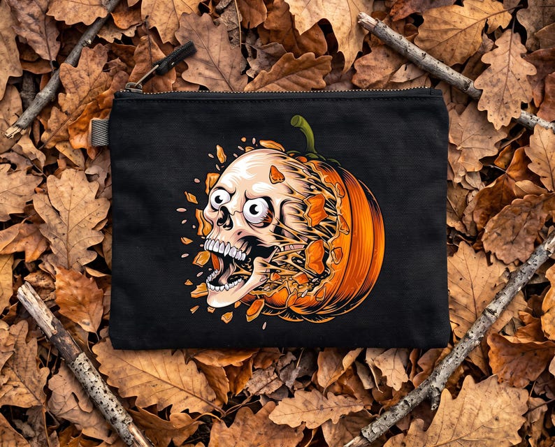 May include: A black zipped pouch featuring a graphic illustration of a human skull emerging from a bright orange pumpkin. The skull has wide eyes and an open mouth, with orange pumpkin fragments appearing to explode outwards from the centre.