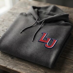 May include: A charcoal gray fleece hoodie featuring a hood with matching drawstrings and a prominent embroidered patch on the chest. The patch displays the letters LU in bold red with white and navy blue outlines, stitched onto the fabric.