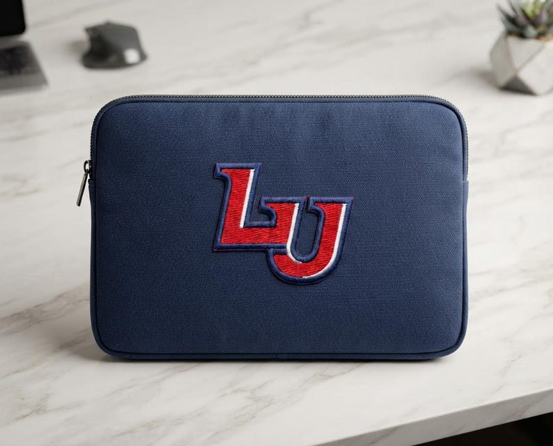 May include: A navy blue rectangular laptop sleeve featuring a centered embroidered logo with the letters LU in red, outlined in white and navy blue. The sleeve has a dark zipper closure along the top edge and a textured fabric exterior finish.