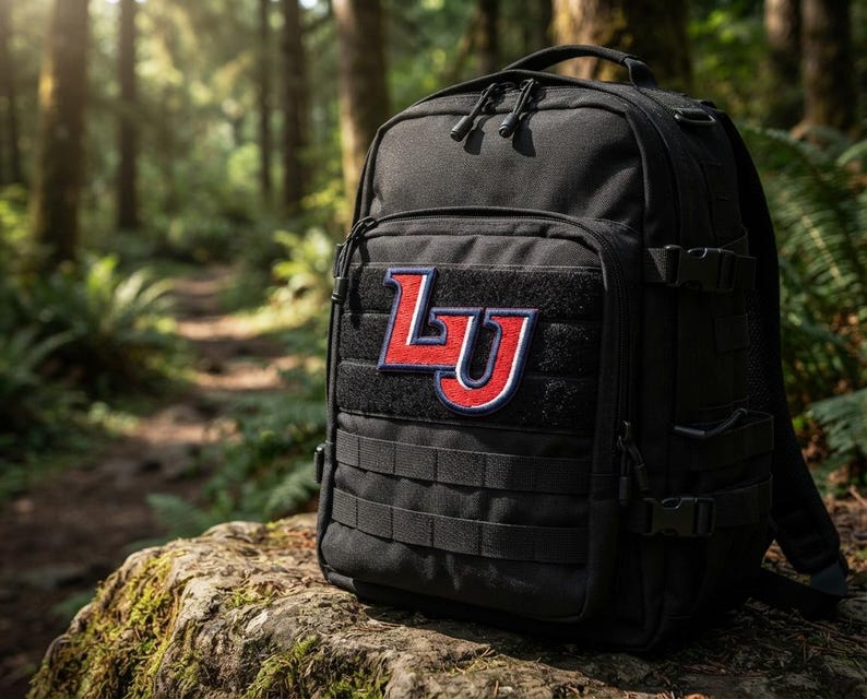 May include: A black tactical backpack featuring a red and white embroidered patch with the letters LU on the front. The bag includes multiple zippered compartments, adjustable side compression straps with plastic buckles, and a modular webbing system.
