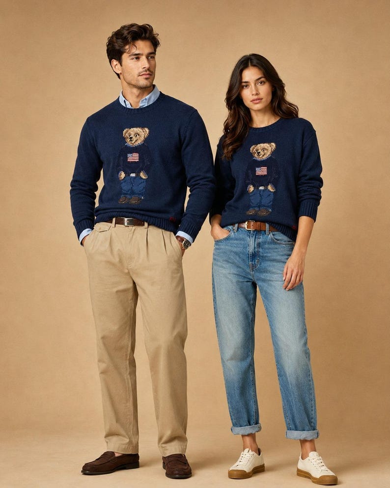 May include: Two navy blue crewneck sweaters featuring a central graphic of a teddy bear wearing a sweater with an American flag design. The sweaters are paired with light blue button-down shirts, khaki trousers, blue jeans, brown loafers, and white sneakers.