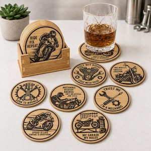 May include: A set of round wooden coasters featuring motorcycle and mechanic-themed engravings, including phrases like Ride Fix Repeat, Born to Wrench, and My Garage My Rules. The coasters are stored in a matching wooden holder, with one coaster placed under a glass of amber liquid.