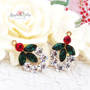 May include: Two gold-tone metal Christmas wreath charms with red and green rhinestones. Each charm features a red rhinestone in the centre, surrounded by green rhinestones, and a circle of clear rhinestones.