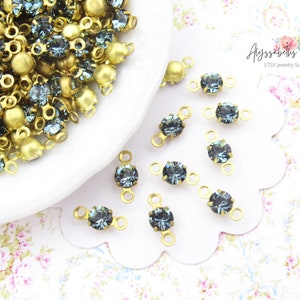 May include: A close-up of a pile of blue and gold rhinestone connectors. The connectors have two loops on either side of the rhinestone. There are also several connectors scattered on a white surface.