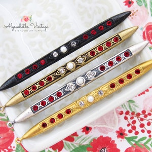 May include: Four decorative metal sticks with red and clear rhinestones, a pearl accent, and a loop at the end.  The sticks are in black, gold, silver, and gold.  Alyssabaths Vintage Etsy Jewelry Supply.