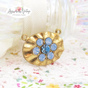 May include: Gold-toned oval pendant with a blue rhinestone in the center surrounded by smaller white rhinestones.  The pendant has a loop at the top for attaching to a chain or cord.