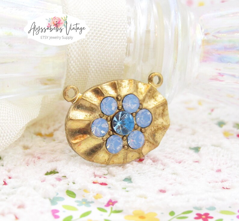 May include: Gold-toned oval pendant with a blue rhinestone in the center surrounded by smaller white rhinestones.  The pendant has a loop at the top for attaching to a chain or cord.