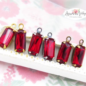 May include: Six red glass pendant charms with gold and silver settings. The charms are rectangular and have a faceted design. They are perfect for jewelry making.