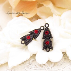 Puede incluir: Dos abalorios de metal de estilo antiguo con detalles de strass rojos. Cada abalorio presenta un dise&ntilde;o de hoja estilizado con tres strass rojos.