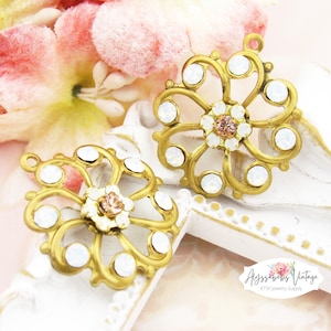 May include: Two gold-tone metal flower-shaped charms with white opal-like stones and a pink rhinestone center.  The charms have a filigree design and are perfect for jewelry making.