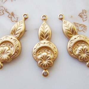 May include: Three gold-toned metal charms with a floral design and a leaf detail. Each charm has a loop at the top and bottom for attaching to jewelry.