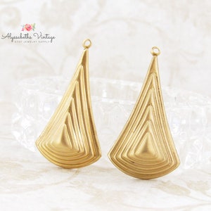 May include: Two gold-toned metal earring blanks with a geometric, triangular shape and a textured, layered design. The blanks have a loop at the top for attaching earring wires.