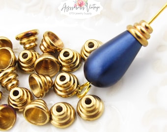 May include: Close-up of gold-colored metal jewelry findings, including cone-shaped beads with spiral detailing and a teardrop-shaped pendant with a dark blue finish. The Etsy shop name "Alyssabeths Vintage" is visible.