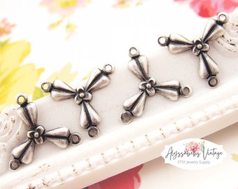 May include: Four silver-toned metal bow-shaped charms with three loops each. The charms have a flower design in the center.