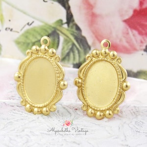 May include: Two gold-toned metal oval-shaped pendant frames with a decorative border and a loop at the top for hanging. The frames are blank and ready to be customized.