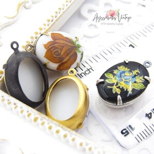 May include: Three oval-shaped metal locket pendants with floral designs. The lockets are in different colors: black, gold, and white. The lockets are about 1 inch in length.