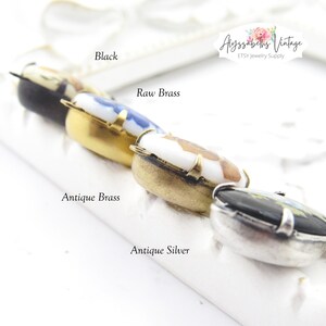 May include: Four different colored metal settings for a pendant or charm. The settings are black, raw brass, antique brass, and antique silver. Each setting has a small porcelain cameo with a floral design.