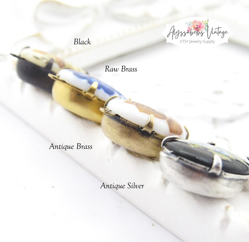 May include: Four different colored metal settings for a pendant or charm. The settings are black, raw brass, antique brass, and antique silver. Each setting has a small porcelain cameo with a floral design.