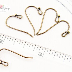 May include: Four antique brass earring hooks with a small ball at the end of each hook. The hooks are approximately 2.5 cm long and are shown next to a ruler.