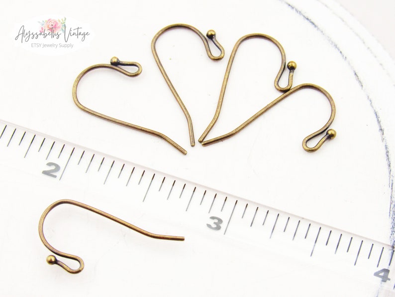 May include: Four antique brass earring hooks with a small ball at the end of each hook. The hooks are approximately 2.5 cm long and are shown next to a ruler.