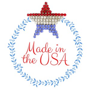 May include: A red, white, and blue star-shaped pin with rhinestones. The star is surrounded by a blue wreath with leaves. The text "Made in the USA" is written in red cursive lettering.