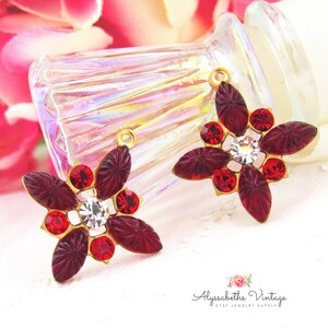 May include: Two gold-tone flower-shaped charms with red and clear rhinestones. Each charm has a loop at the top for attaching to jewelry.