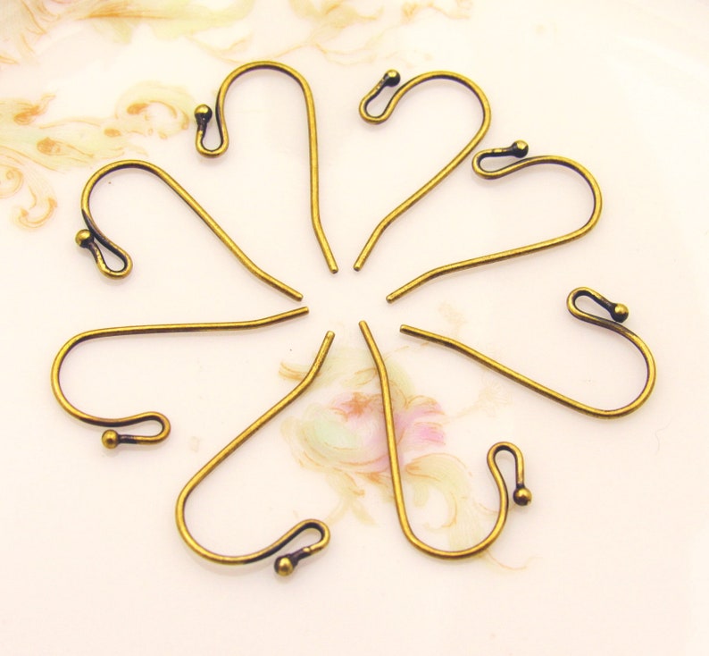 May include: Eight antique brass earring hooks with a rounded loop at the top and a small ball at the bottom.