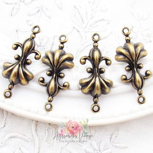 May include: Four antique gold-toned metal connector charms with a fleur-de-lis design. Each charm has two jump rings for attaching to jewelry.
