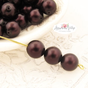 May include: A strand of dark brown pearl beads strung on a gold wire. The beads are round and have a smooth, glossy finish.