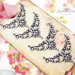May include: Four silver-toned metal corner embellishments with a decorative floral design.  The embellishments are arranged in a row on a brown paper tag with the text "Alyssabeth's Vintage ETSY Jewelry Supply".