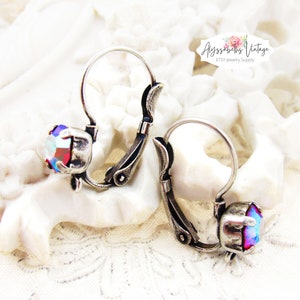 May include: A pair of silver hoop earrings with a red and blue iridescent crystal on each earring. The earrings have a decorative design on the hoop.