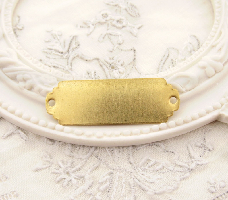 May include: A gold-toned metal tag with rounded corners and two small holes at the top. The tag is blank and ready for personalisation.