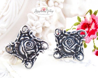 May include: Two silver-toned metal rose charms with intricate details. Each charm features a raised rose design with a swirl pattern in the centre. The charms have four loops for attaching to jewellery or other crafts.