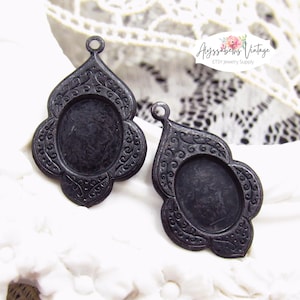 May include: Two black metal pendant trays with ornate filigree designs. The trays are oval shaped and have a raised edge. They are perfect for adding a touch of vintage charm to your jewelry making projects.