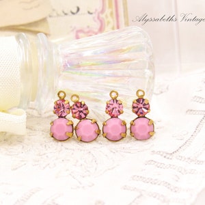 May include: Three gold-tone charms with pink glass stones. Each charm features a larger pink glass stone with a smaller pink glass stone on top.