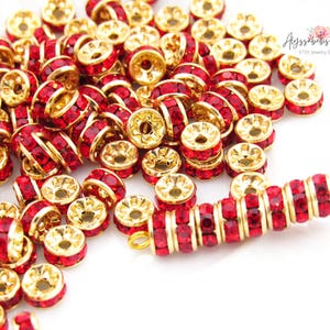 May include: A large quantity of red rhinestone beads with gold settings. The beads are arranged in a pile and a few are strung on a gold wire.