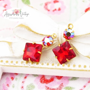 Pode incluir: Dois achados de brincos em tom dourado com pedras de imitação quadradas vermelhas e transparentes iridescentes.