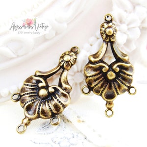 May include: Two antique gold-toned metal flower-shaped pendant charms with three jump rings each. The charms have a detailed design with a raised center and a scalloped edge.