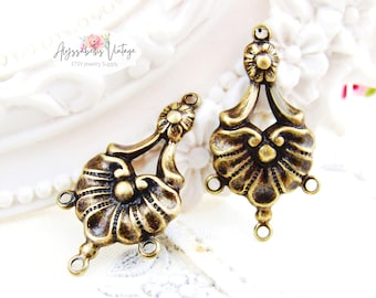 Puede incluir: Dos colgantes de flor en forma de flor de metal dorado antiguo con tres anillos de salto cada uno. Los colgantes tienen un diseño detallado con un centro elevado y un borde festoneado.