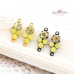 Könnte beinhalten: Vier Schmuckanhänger im Vintage-Stil. Zwei sind goldfarben mit hellgrünen und gelben Kristallen, und zwei sind dunkelbronze mit ähnlichen Kristallen. Die Anhänger sind in einem Traubendesign angeordnet. Der Etsy-Shop-Name ist sichtbar.