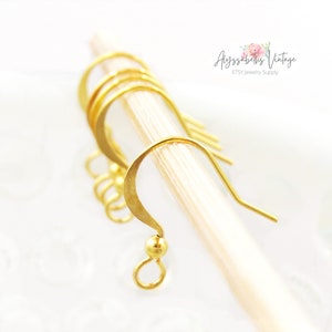 May include: Gold-toned earring hooks with a small ball at the end. The hooks are made of metal and are designed for use in jewelry making.