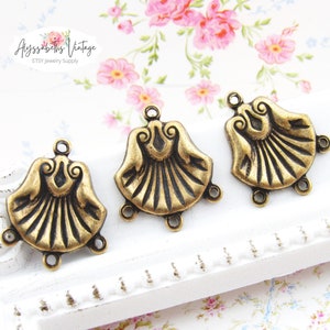 May include: Three antique gold-toned metal shell-shaped pendant charms with three jump rings each. The charms have a detailed design and are perfect for jewelry making.